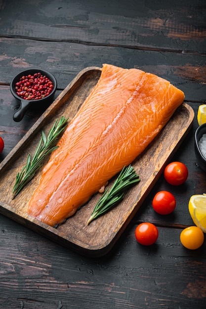 Whole raw salmon fillet on wooden dark planks.