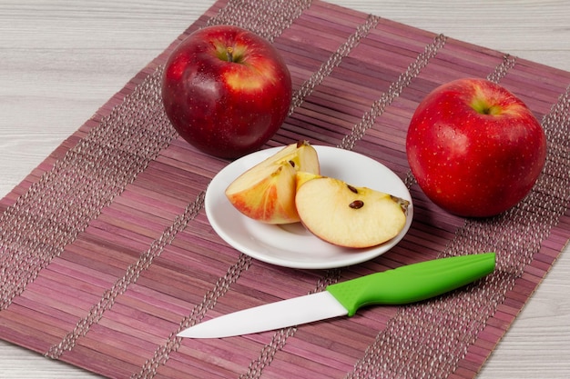 Whole red apples and sliced one on the saucer with a knife on the bamboo napkin