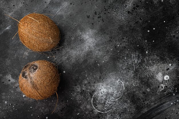 Whole ripe fresh Coconut set, on black dark stone table background, top view flat lay, with copy space for text