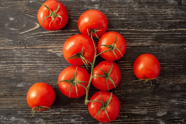 Whole ripe red tomatoes on a branch on a black background. Top view.