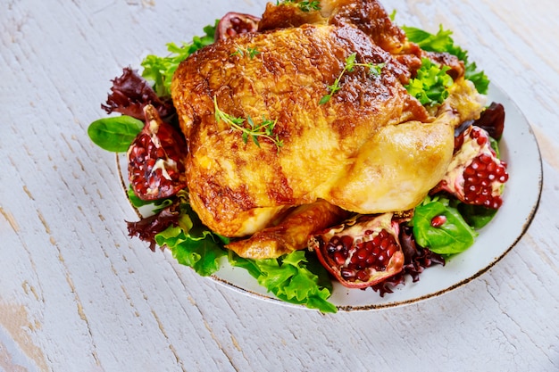 Whole roasted chicken on plate with salad and pomegranate