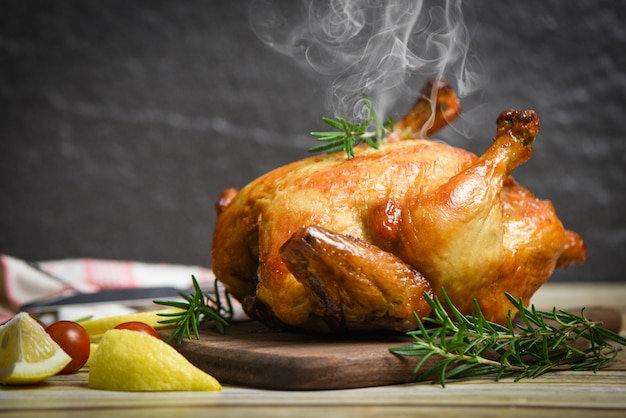 Whole roasted chicken rosemary and tomato lemon on wooden cutting board - Baked chicken grilled barbecue delicious food on dining table at holiday celebrate