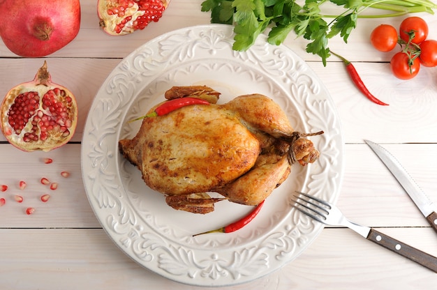 Whole roasted chicken with bound feet in a bowl of hot chilli pepper and pomegranate 