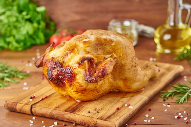 Whole roasted chicken on wooden cutting board on dark brown wooden table