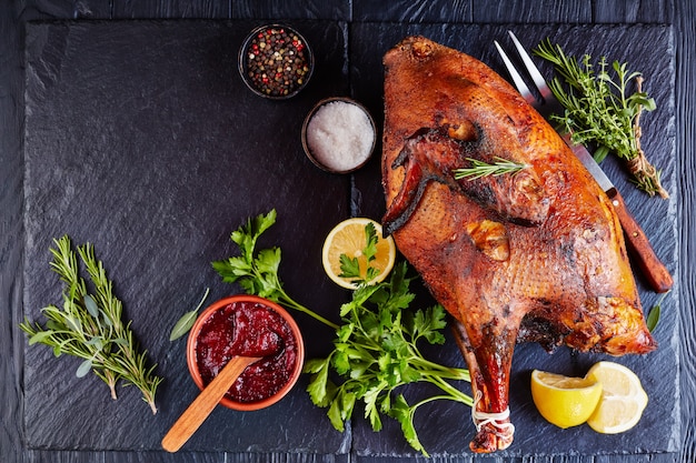 Whole roasted free range turkey on a black slate tray with rosemary sage thyme bouquet, cranberry sauce, flat lay, view from above