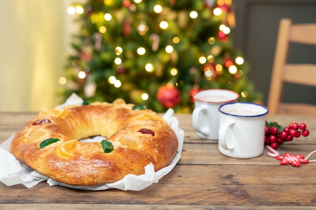 Whole RoscÃ³n de Reyes on wooden table with Christmas tree in the background. Christmas sweets.