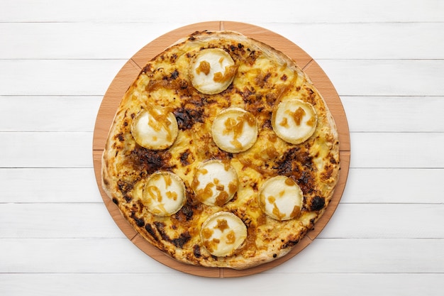 Whole round pizza topped with goat cheese and caramelized onion on wooden plate top view on white bo...