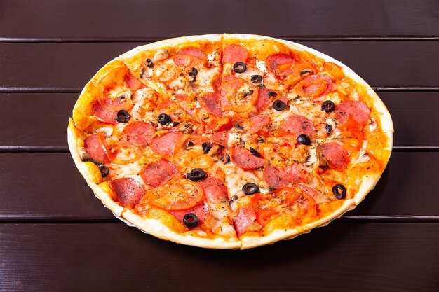 A whole rustic pizza with mozzarella, salami, tomato, olives, mushrooms and basil