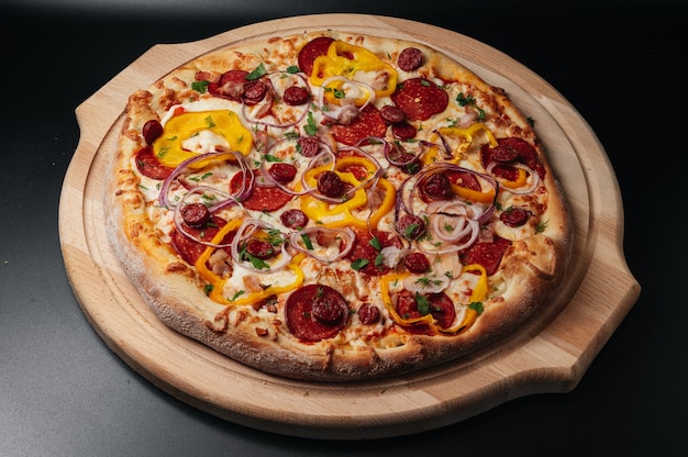 Whole rustic Pizza with salami hunting sausage jalapeno pepper onion Rings served on wooden plate