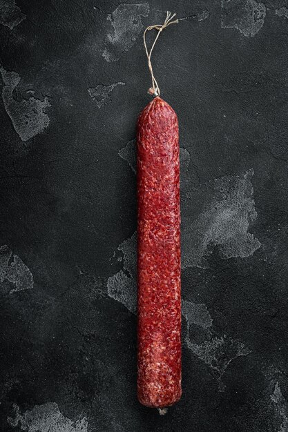 Whole sausage salami on black dark stone background top view flat lay with copy space for text