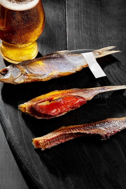 Whole and skinned salted sundried roach with roe served with pale lager on black background