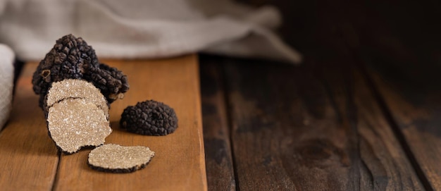 Whole and sliced black truffles mushroom on wooden board on dark brown table close up