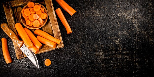 Whole and sliced carrots on a wooden tray