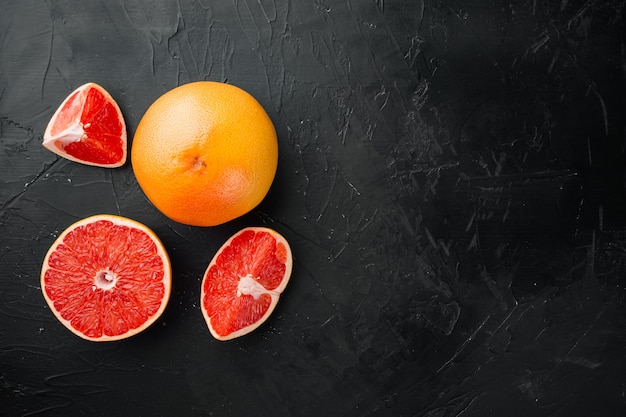 Whole and sliced grapefruits set, on black dark stone table background, top view flat lay, with copy space for text