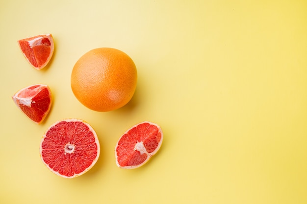 Whole and sliced grapefruits set, on yellow textured summer background, top view flat lay, with copy space for text