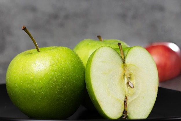 Whole and sliced green apple on black plate