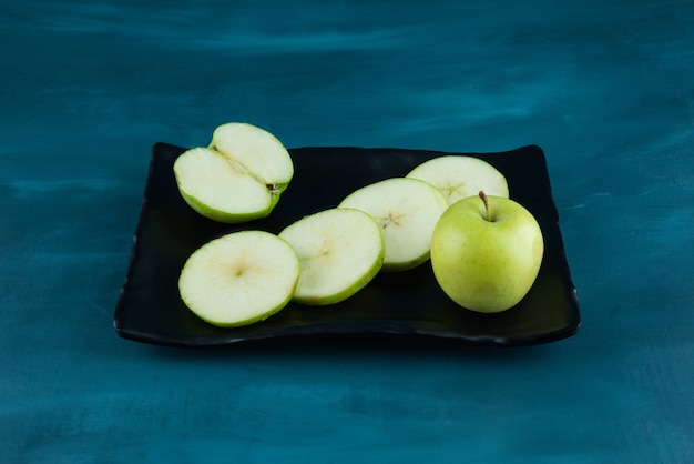 Whole and sliced green apple fruit placed on a dark tray .