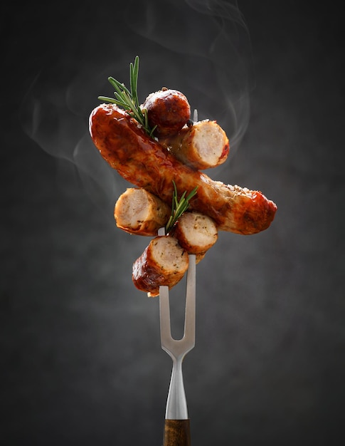 A whole and sliced grilled hot fried sausage is strung on a meat fork