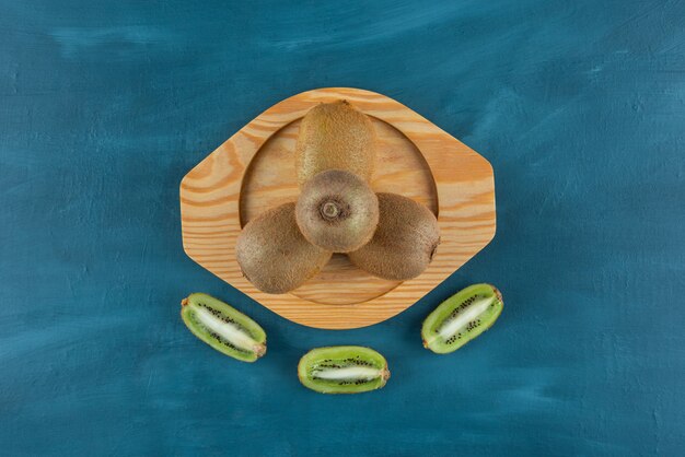 Whole and sliced kiwi fruits placed on a wooden board.