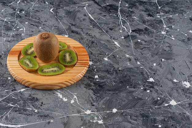 Whole and sliced kiwi fruits placed on a wooden board.