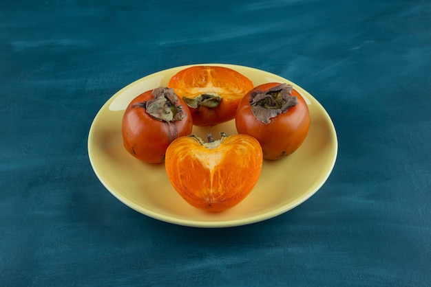 Whole and sliced persimmon fruit placed on a yellow plate .