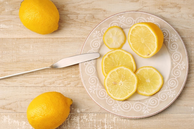 Photo whole and sliced yellow lemons on a plate on a wooden