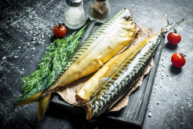 Whole smoked mackerel on a cutting Board with greens tomatoes and spices