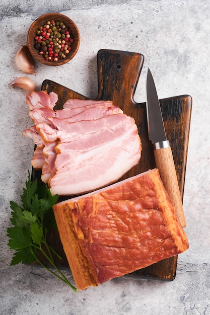 Whole Smoked Slab Bacon Brisket Sliced smoked gammon on a wooden table with rosemary parsley pepper salt and garlic on old gray concrete table background Copy space