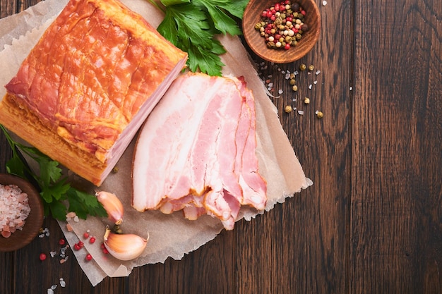 Whole Smoked Slab Bacon Brisket Sliced smoked gammon on a wooden table with rosemary parsley pepper salt and garlic on wooden stand and old table Copy space