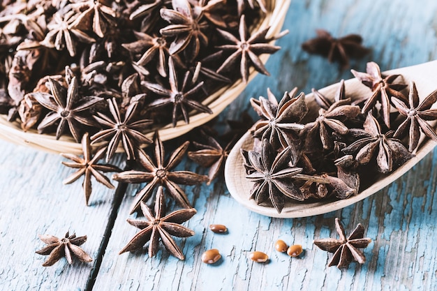 Whole star anise in a basket and spoon with seeds on blue rustic wooden background, indian spice.