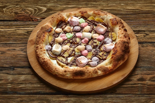 Whole sweet pizza served with marshmallows and candies on wooden background