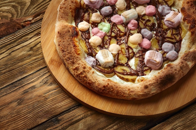 Whole sweet pizza served with marshmallows and candies on wooden background