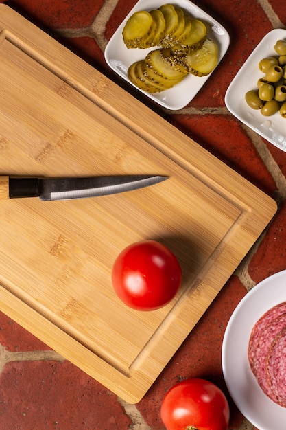 A whole tomato and a knife on a cutting board Nearby are pickled cucumbers