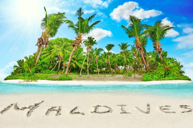 Whole tropical island within atoll in tropical Ocean. Uninhabited and wild subtropical isle with palm trees. Inscription "Maldives" in the sand on a tropical island,  Maldives.