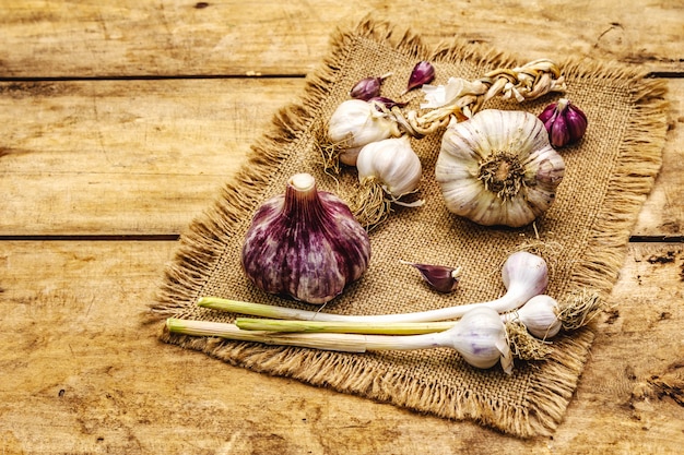 Whole unpeeled garlic heads and cloves. New harvest, on sackcloth, wooden boards background, copy space