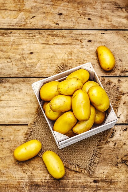 Whole unpeeled raw potatoes in a wooden crate. New harvest, on sackcloth, wooden boards background