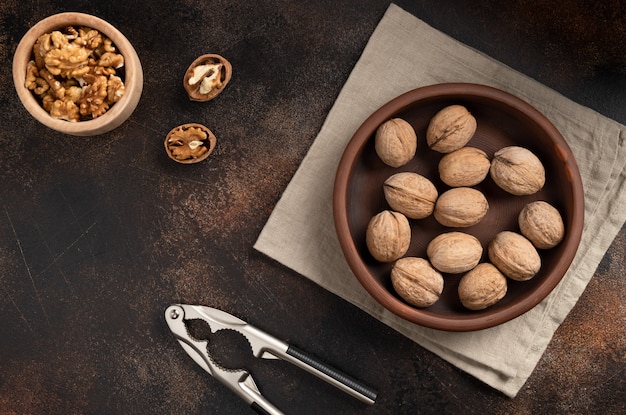 Фото Целые грецкие орехи в миску, щелкунчик и ядра на коричневой бетонной стене. органическая еда