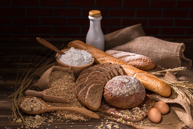 Хлеб из цельной пшеницы, молоко, мука и ткани мешок на деревянный стол.