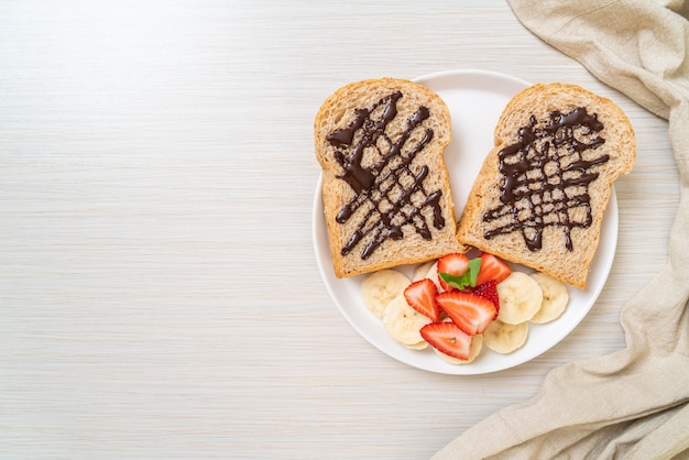 朝食用の新鮮なバナナ、イチゴ、チョコレートでトーストした全粒小麦のパン