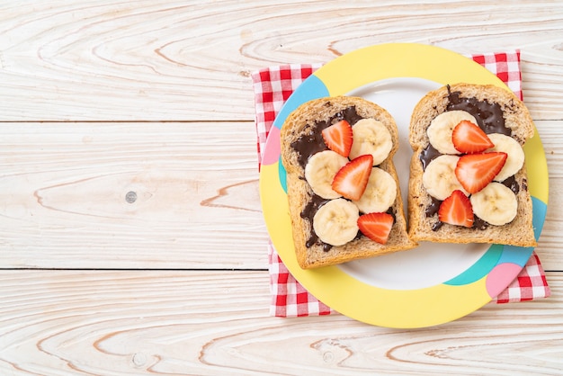 Pane integrale tostato con banana fresca, fragole e cioccolato per colazione