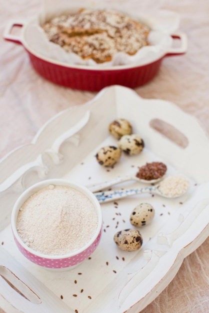 Whole wheat bread with sesame seeds and flax seeds in baking form on a light background Fresh quail eggs seeds and flour on a wooden tray