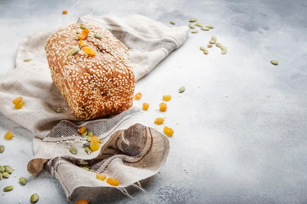 Whole wheat organic rye dark bread with pumpkin seeds dried fruit raisins and sesame seeds on gray towel on the kitchen table background top view Space for text