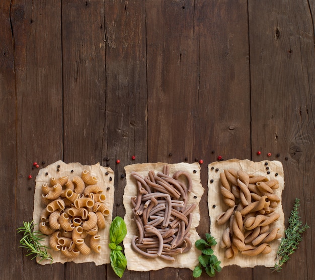 Whole wheat  pasta and herbs on a wooden table, top view with copy space