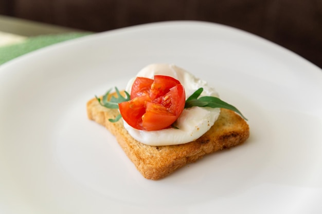 Pane tostato integrale con rucola di pomodoro uovo in camicia e formaggio su piatto bianco