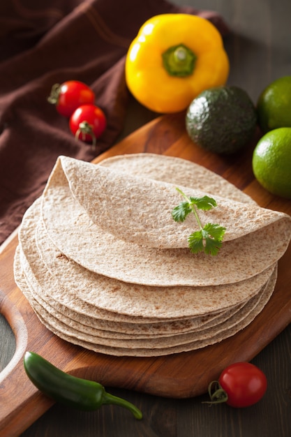 Whole wheat tortillas on wooden board and vegetables