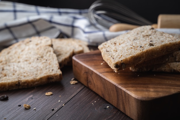 Photo whole wheat, whole grains bread on dark wooden board, close up, top view