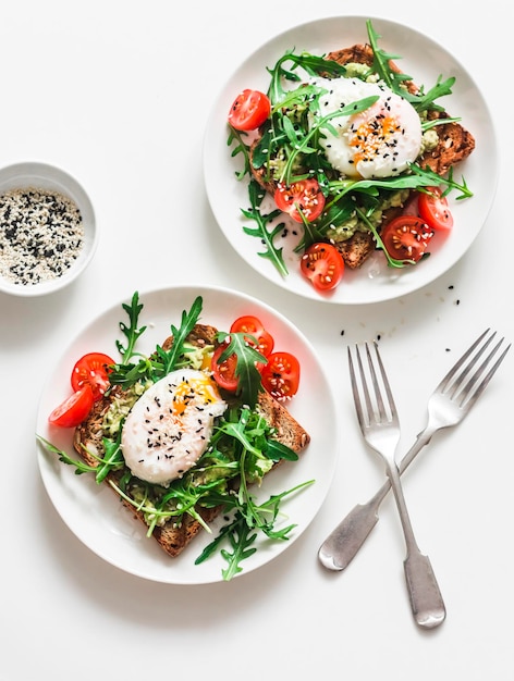 Wholegrain bread sandwiches with avocado poached egg and arugula cherry tomatoes salad delicious healthy breakfast brunch on a light background top view