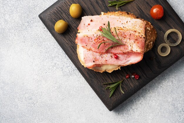 Wholegrain bread sandwiches with cream cheese, bacon on a wooden cutting Board. Gray concrete table Copy space.