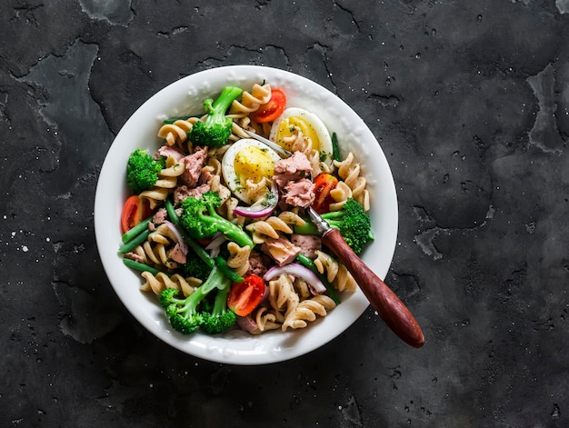 Wholegrain pasta broccoli tuna string beans boiled egg salad on a dark background top view Healthy eating concept