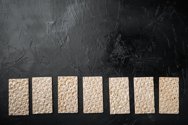 Set di cracker di pane croccante di segale integrale, su sfondo nero tavolo in pietra scura, vista dall'alto piatta, con copia spazio per il testo